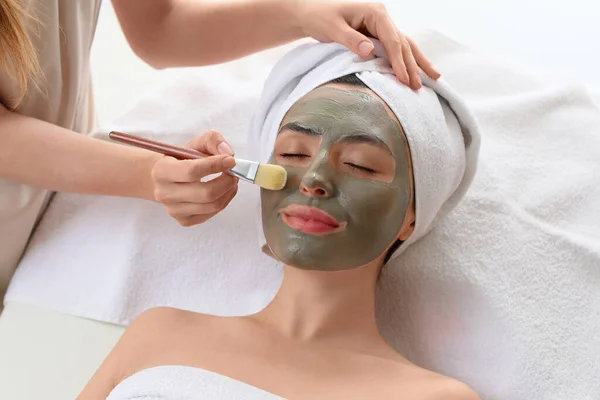 Cosmetoloog Aanbrengen Van Klei Masker Het Gezicht Van Jonge Vrouw — Stockfoto