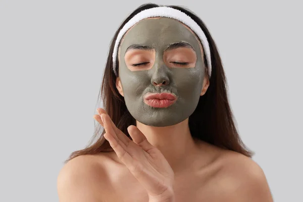 Jonge Vrouw Met Toegepaste Klei Masker Blazen Kus Grijze Achtergrond — Stockfoto