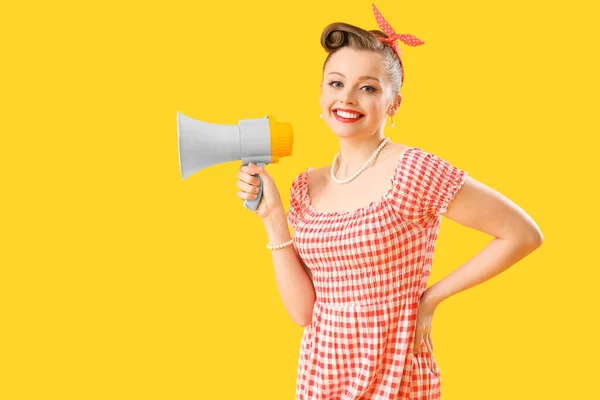 Young pin-up woman with megaphone on yellow background