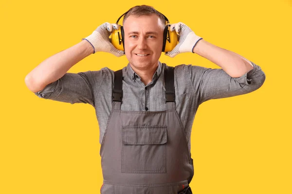 Mature carpenter in hearing protectors on yellow background