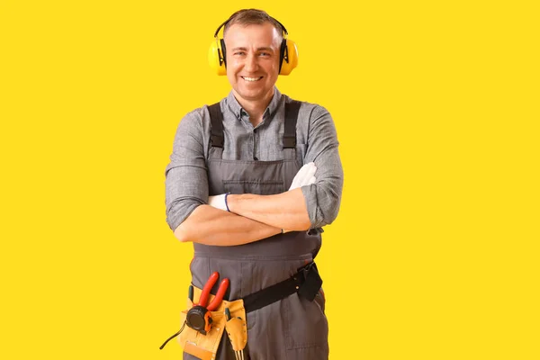Mature carpenter in hearing protectors on yellow background