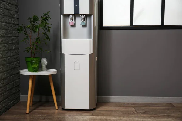 Modern water cooler and houseplant on stool near black wall