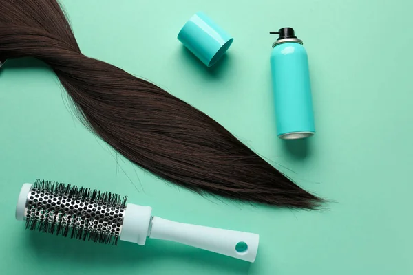Bottle of hair spray, brush and strand on color background