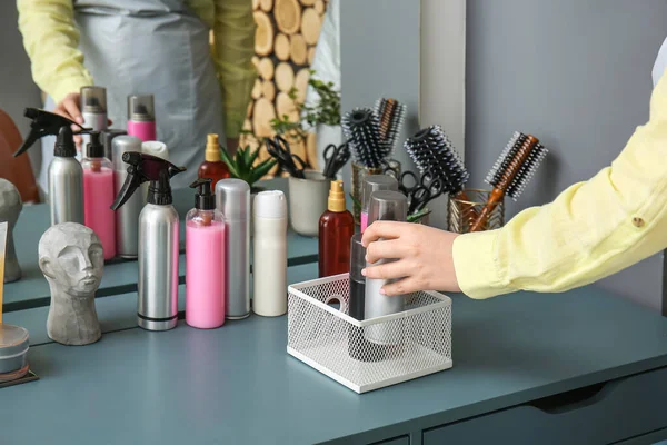 Woman putting bottle with hair spray on table in beauty salon, closeup