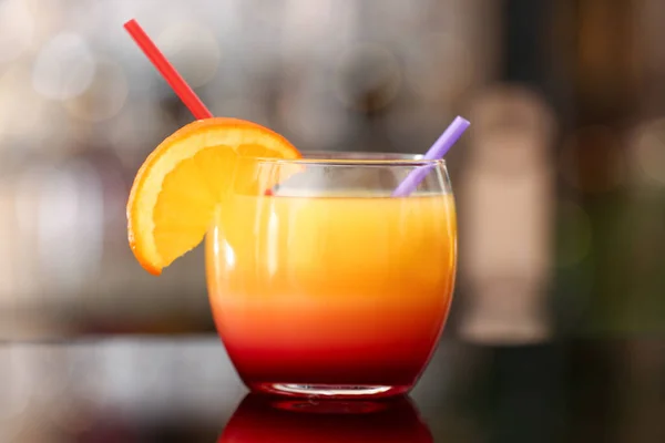 一杯美味的龙舌兰日出与橙片和稻草在酒吧的桌子上 — 图库照片