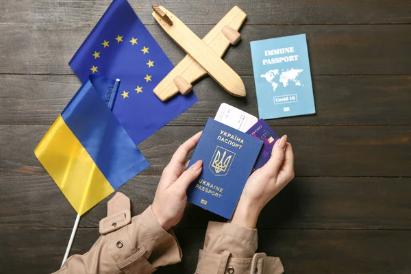 Woman with passports, toy airplane, flags of Ukraine and European Union on black wooden background