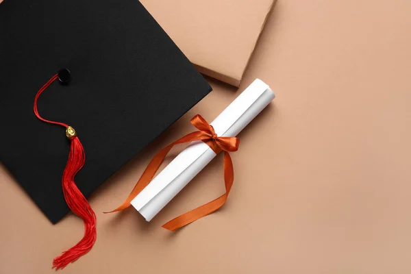 stock image Diploma with red ribbon, graduation hat and book on brown background