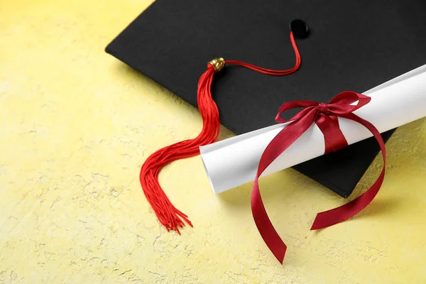 Δίπλωμα Κόκκινη Κορδέλα Και Καπέλο Αποφοίτησης Κίτρινο Τραπέζι — Φωτογραφία Αρχείου