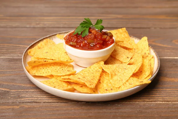 stock image Plate with nachos and bowl of delicious salsa sauce on brown wooden table