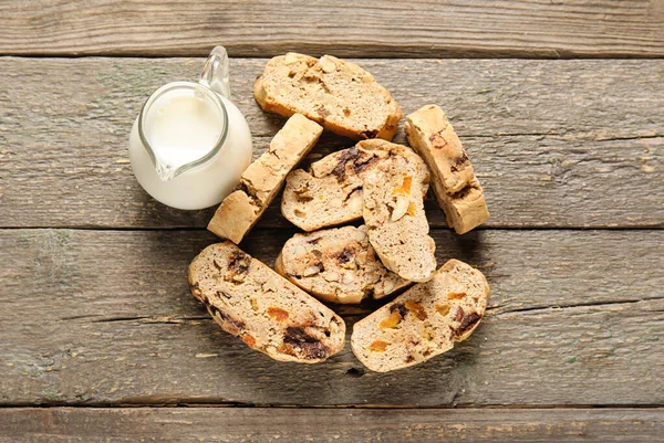 Delicious biscotti cookies and pitcher with milk on wooden background