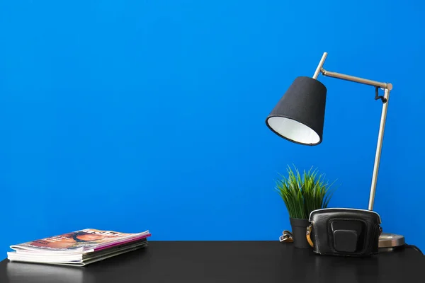 Workplace with magazines, lamp and camera case near blue wall