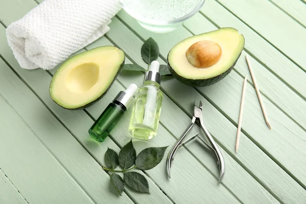 Composition with bottles of cuticle oil, manicure instruments, towel and avocado on color wooden background
