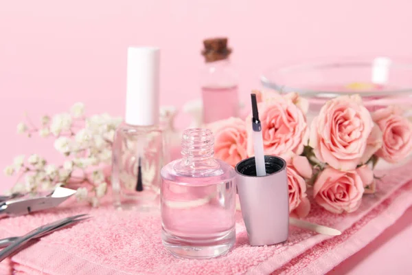 Composition with bottles of cuticle oil, manicure instruments and flowers on pink background, closeup