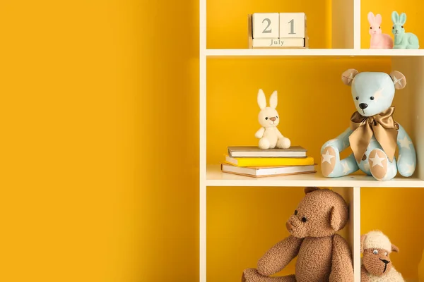 Bookshelf with baby toys near yellow wall