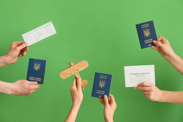 Frame made of female hands, Ukrainian passports, ticket, wooden airplane and negative covid-19 test result on green background
