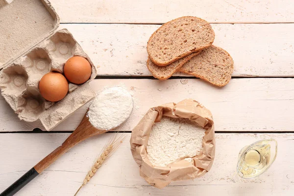 Composition with bag of wheat flour, eggs, bread pieces and spoon on white wooden table