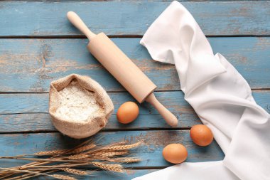 Bir torba un, yumurta, buğday kulağı ve mavi ahşap masa üzerinde merdane.