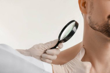 Dermatolog beyaz arka planda büyüteci olan genç adamın mol incelemesi yapıyor.