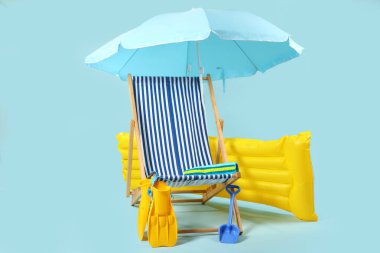 Güverte sandalyesi, mavi şemsiye ve mavi arka planda plaj aksesuarları.