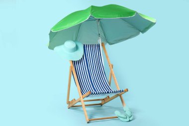Güverte sandalyesi, yeşil şemsiye ve mavi arka planda plaj aksesuarları.