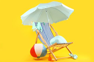 Güverte sandalyesi, mavi şemsiye ve mavi arka planda plaj aksesuarları.