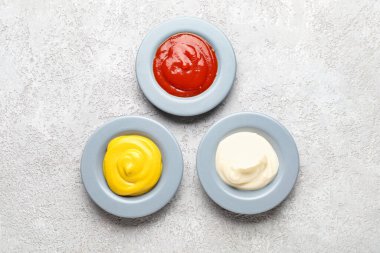 Gri grunge masasında ketçap, mayonez ve hardal tabakları.