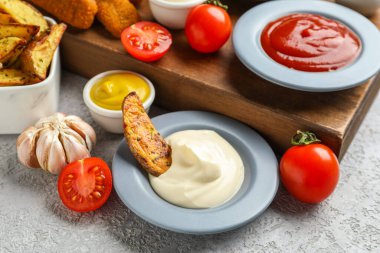 Farklı soslu kompozisyon ve gri grunge masasına batırılmış patates dilimi.