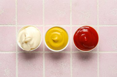 Bir kase ketçap, mayonez ve hardal pembe döşemeli masa, yakın plan.