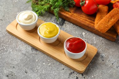 Farklı soslu kompozisyon, balık nugget, domates ve otlar gri grunge masasında.