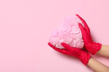 Pembe arka planda kalp yastığı olan lastik eldivenli bir kadın.