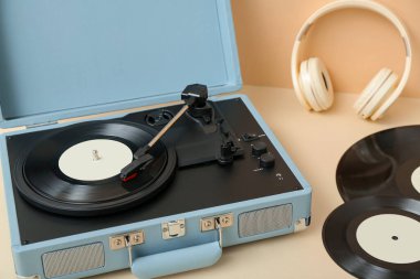 Bej duvarın yanındaki masada vinil diskleri ve kulaklıkları olan bir plak çalar.