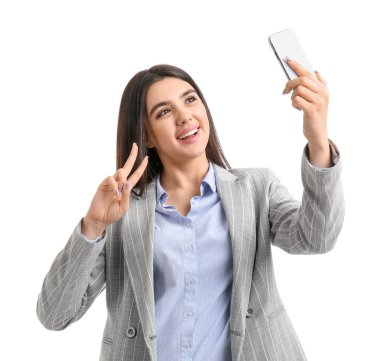 Akıllı telefonlu güzel genç bir kadın beyaz arka planda selfie çekiyor.