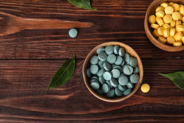 Kaseler dolusu hap ve yapraklar koyu ahşap masada.