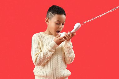Kırmızı arka planda telefonla konuşan küçük Afro-Amerikalı çocuk.