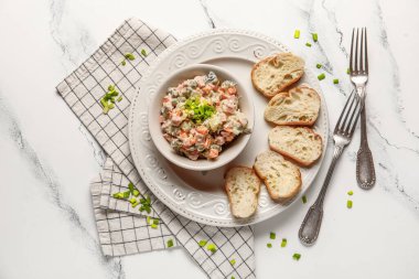 Bir kase lezzetli Olivier salatası ve beyaz mermer arka planda ekmek.