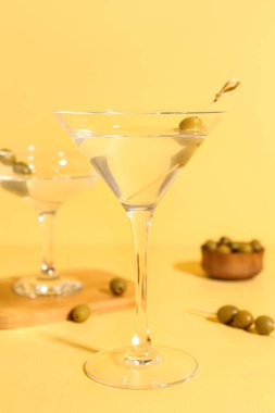 Sarı arka planda zeytinli bir bardak martini.