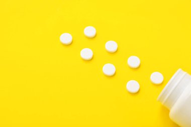 Sarı arka planda beyaz haplı şişe, yakın plan.