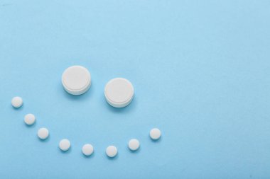 Mavi arka planda beyaz haplardan yapılmış gülümseme