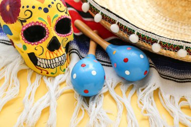 Meksika marakaları boyalı kafatası, şapkası ve sarı arka planda serapı, yakın plan.