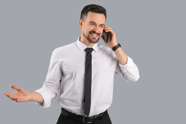 灰色の背景に携帯電話で話すハンサムなビジネスマン — ストック写真