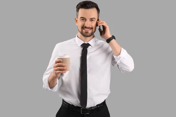 Красивый Бизнесмен Чашкой Кофе Разговаривает Мобильному Телефону Сером Фоне — стоковое фото