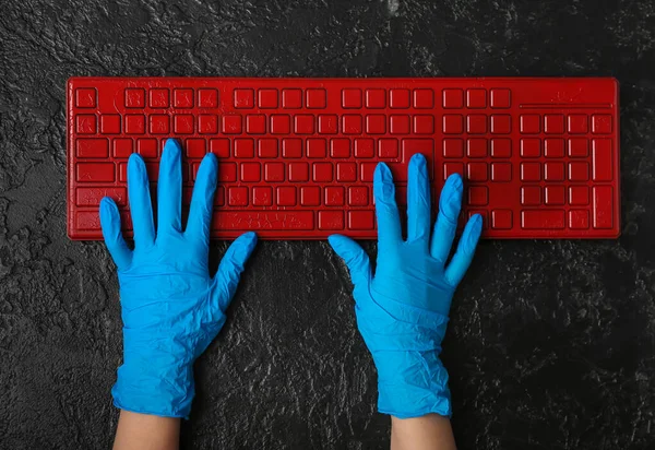 Woman in rubber gloves with computer keyboard on dark background
