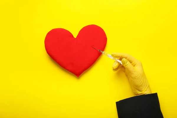 Woman in rubber glove with syringe and heart pillow on yellow background