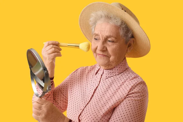 Seniorin Mit Schminkpinsel Und Spiegel Auf Gelbem Hintergrund Nahaufnahme — Stockfoto