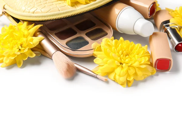 Cosmetic bag with makeup products and flowers on white background, closeup
