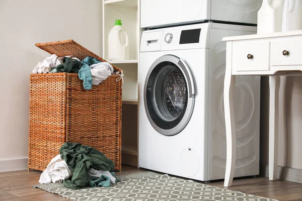 Basket with dirty clothes near washing machine in laundry room