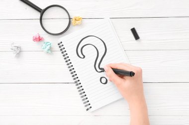 Beyaz ahşap arka plana not defterine soru işareti çizen kadın