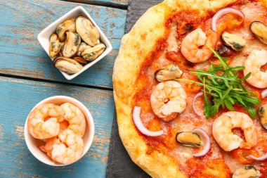Lezzetli deniz ürünleri pizzası ve mavi ahşap arka planda malzemeleri olan tahta tahta tahta, yakın plan.