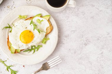 Hafif arka planda kızarmış yumurta, roka ve avokado ile nefis sandviç.