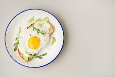 Gri arka planda kızarmış yumurta, avokado ve roka ile nefis bir sandviç.